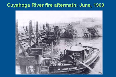 Cuyahoga River fire aftermath: June, 1969. Photo shows firefighters aboard a fireboat in the river, as they are putting out fires in the smoldering ruins of a structure.
