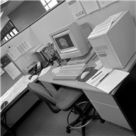 Picture shows an office cubicle with desk and computer (in black and white).